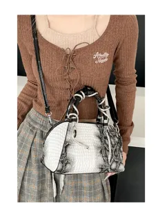 Vista detallada del bolso de mano tipo concha con motivo de serpiente y asa de metal para mujer.