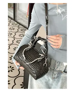Vista detallada del bolso con diseño de cocodrilo negro y asa con garra de metal.