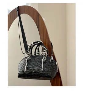 Detalle de bolso negro de cocodrilo con asa de serpiente plateada única y moderna.