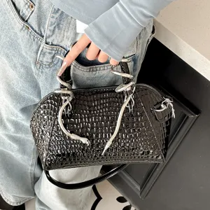 Bolso de mano tipo concha en charol negro con diseño de cocodrilo y asas de serpiente.