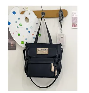 Detalle de bolso de lona negro con múltiples bolsillos, asas superiores y correa larga.