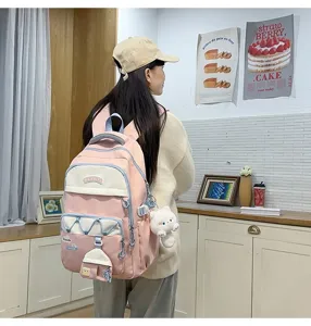 Detalle de mochila escolar de lona rosa y blanca con bolsillos delanteros y colgante.