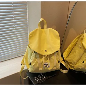 Detail shot of a casual yellow canvas backpack with front flap, drawstring and straps.