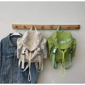 Detailed view of casual nylon multi-pocket backpacks hanging on wooden wall rack setup.