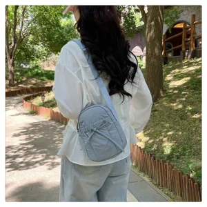 Detail view of the lightweight nylon crossbody bag with bow accent in outdoor park setting.
