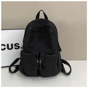 Detailed view of the black canvas backpack featuring front zipper pockets and top carry handle.