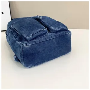 Close-up detail showing the classic blue denim backpack with dual front pockets and material.