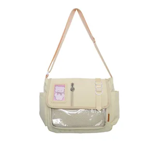 Detail view of beige ita-bag messenger bag featuring a clear window and cute bear patch.