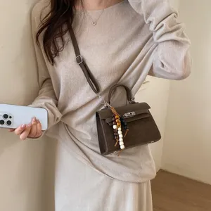 Detailed view of women's stylish brown crossbody Kelly bag with lock closure and chic bead strap.