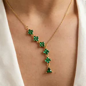 Detail shot of a golden stainless steel necklace with green clover and triangle gemstones.
