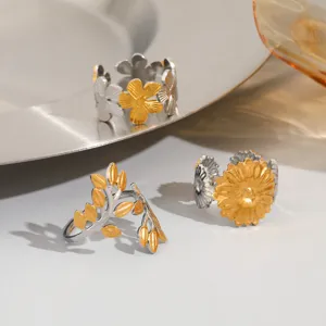 Close-up detail of stainless steel open rings with flower and leaf designs in silver and gold.