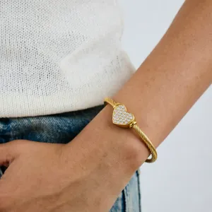 Gedetailleerde close-up van een gouden kabel getwist armbandje met een sprankelend kristallen hart.
