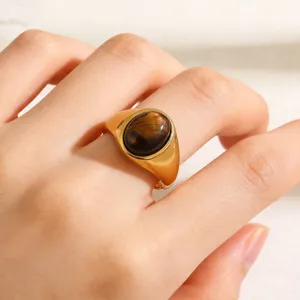 Detail shot of minimalist stainless steel signet ring with oval brown stone on finger.