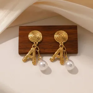 Close-up view of retro gold-tone earrings featuring spiral stud, letter A and pearl.