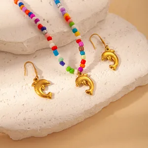 Detailed close-up of a colorful beaded necklace and dolphin earrings set on a textured white stone.