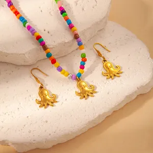 Close-up of colorful beaded necklace and gold octopus earrings set on textured stone display.