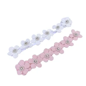 Detail van babyhoofdband met stoffen bloemen, voorzien van parels en strasssteentjes.