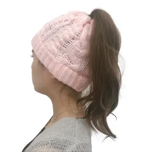 Dettaglio di profilo di un berretto in maglia rosa con texture a trecce e foro superiore.