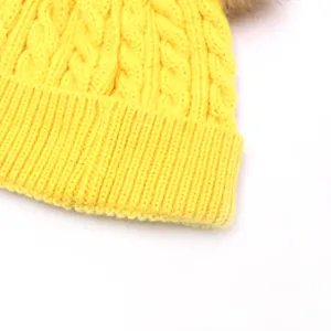 Detailed view of yellow cable knit baby winter hat with fluffy pom-pom decoration.