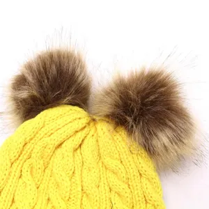 Detail view of yellow knitted baby hat with dual fluffy brown fur pom poms texture.