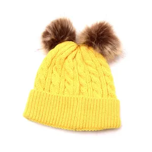 Closeup detail of bright yellow kids winter knitted beanie hat with fluffy double fur pom poms.