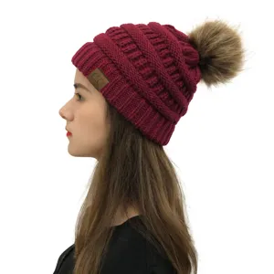 Detailansicht der Damen Winter Strickmütze in Burgunderrot mit flauschigem Bommel und Logo Patch.