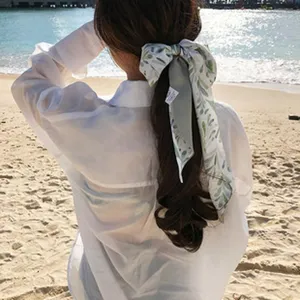 Detailaufnahme des grünen Blätter-Druck-Haarbandes am Zopf am Strand. Schönes Accessoire.