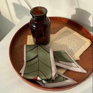 Foulard en soie vert avec imprimé de feuilles géométriques, élégant ruban pour le cou.