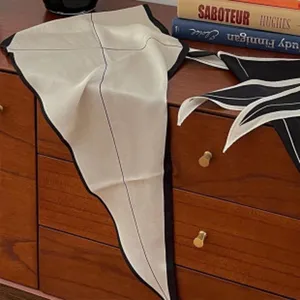 Detailaufnahme von eleganten schwarz-weißen Seidenbandschals auf einem Holztisch.