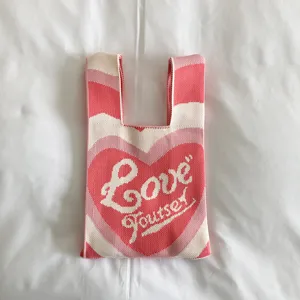 Pink knitted tote bag with heart pattern and cute script text for stylish spring casual wear.
