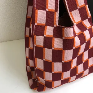 Detailansicht einer gestrickten karierten Tragetasche in Bordeaux, Rosa und Orange. Weiche Textur.