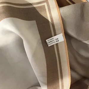 Close-up detail of luxury silk scarf showing soft fabric texture and size label clearly.