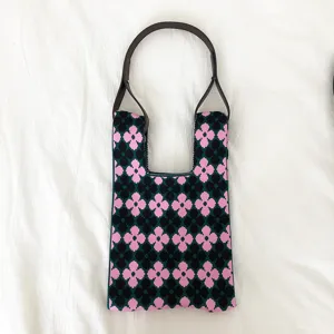 Stricktasche mit Blumenmuster Detail, schwarzes Strickgewebe und rosa Kleeblumen.