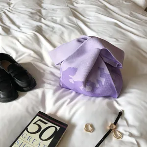 Detaillierte Ansicht einer stylischen lila Strickhandtasche mit Knotengriff auf Bett.
