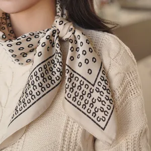 Close-up detail shot of a beige silk square scarf featuring black horseshoe print, neck wear.