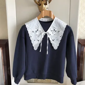 Detailaufnahme eines dunkelblauen Sweatshirts mit weißem Spitzenkragen und Stickerei.