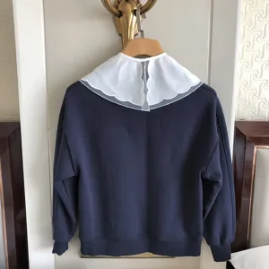 Detailansicht eines dunkelblauen Sweatshirts mit grossem weissen Spitzenkragen mit Stickerei.