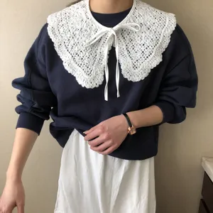Detailaufnahme des weißen Spitzen-Aufsatzkragens mit eleganter Schleife auf dunklem Pullover.