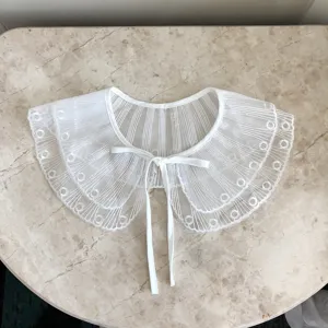 Detaillierte Nahaufnahme eines weissen Spitzenkrauses mit feiner Stickerei und Schleife.