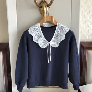Nahaufnahme des exquisiten weißen Spitzenkragens mit Stickerei kombiniert mit marineblauem Pullover.