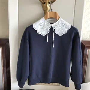 Detailansicht eines blauen Sweatshirts mit detailreicher weisser Spitzenkragen und Schleife.