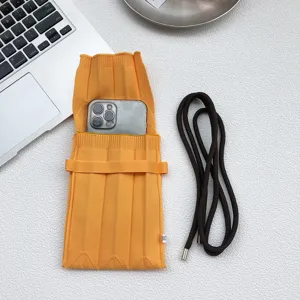 Detailansicht der gelben plissierten Strick Handytasche mit braunem Gurt auf dem weißen Tisch.
