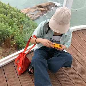 Detailansicht der stilvollen orangen Plissee-Umhängetasche in Outdoor-Lifestyle-Umgebung.
