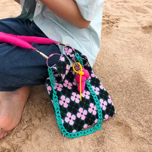 Detailansicht der stilvollen gestrickten Blumentasche mit grünem Kettengriff und pinkem Gurt.