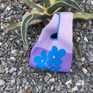 Nahaufnahme einer lila Stricktasche mit blauem Blumenmuster auf Schotterhintergrund.