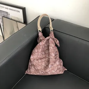 Detailansicht der stilvollen Stoffhandtasche mit Paisley-Muster und hellem Griff auf dunklem Sofa.