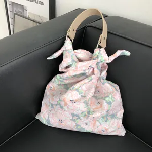 Detailansicht einer schicken Handtasche aus Stoff mit Blumenmuster und Ledergriff.