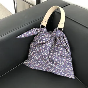 Stoffhandtasche Detail mit blauem Blumenmuster, Ledergriff und runden Metallringen.