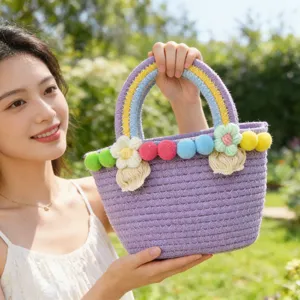 Handmade purple woven handbag featuring colorful pom-poms and rainbow handles, ideal for summer.