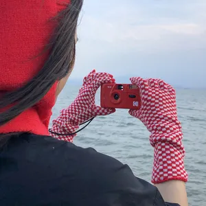 Detailed shot of red and white checkerboard knitted gloves worn outdoors by the sea.